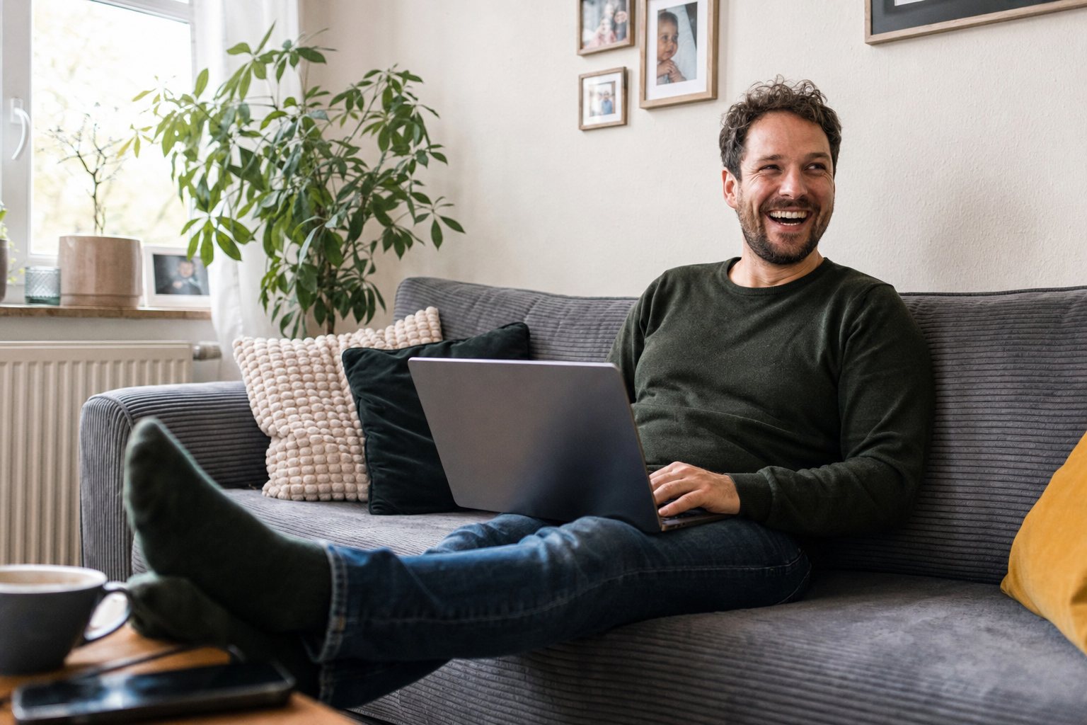 Lachender Mann mit Laptop auf dem Sofa